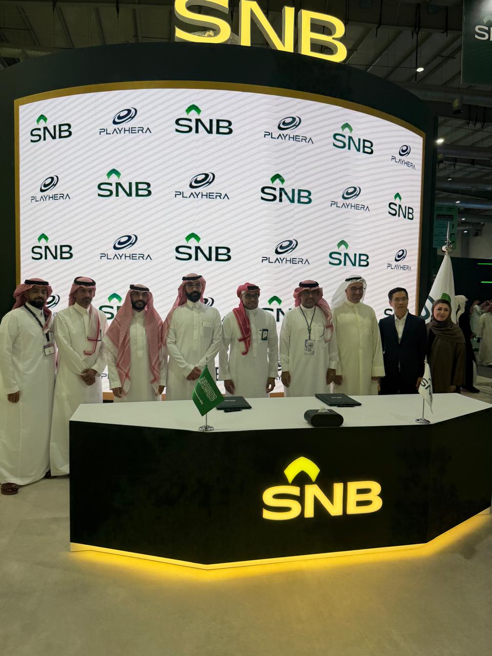 Playhera and SNB teams at the partnership signing, in front of the SNB and Playhera backdrop